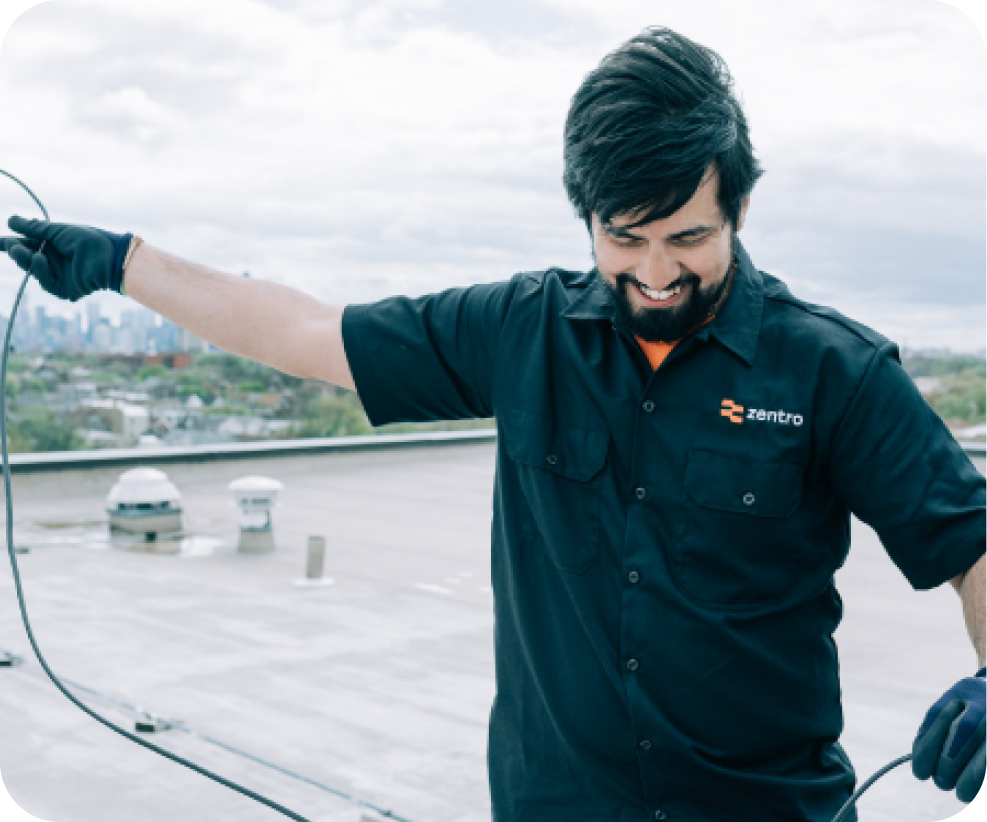 Zentro technician installing internet equipment on apartment building rooftop with city skyline background